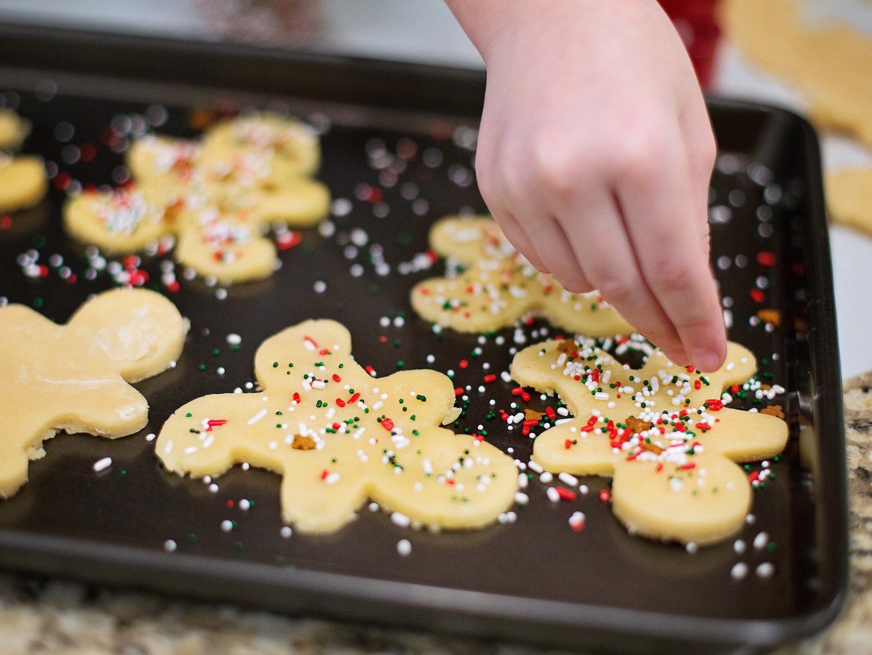 Person decorating Christmas cookies on a cookie sheet.