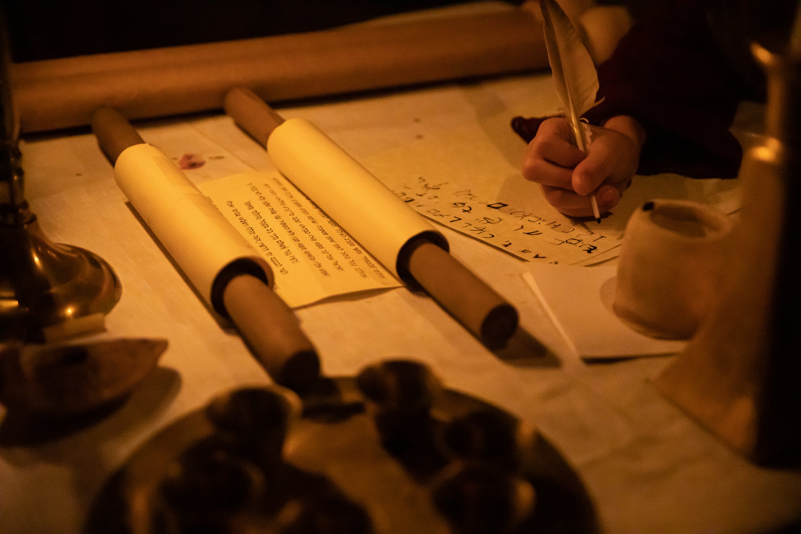 Person writing with a quill pen on a scroll.