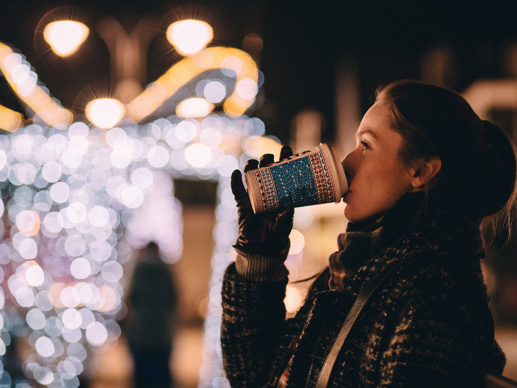 Woman drinking hot chocolate outside at night during Christmas time.